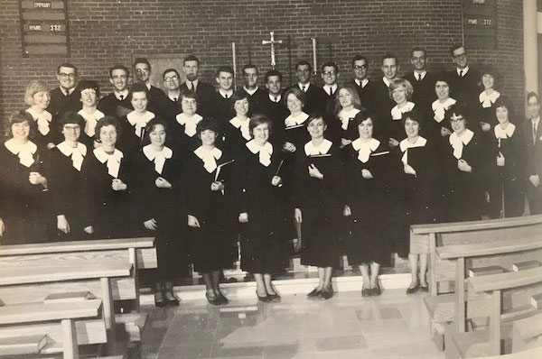 A group shot of a choir wearing robes at the front of a church.